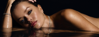 Close up of model lying in water, wearing logan hollowell diamond bracelets, earrings and necklaces